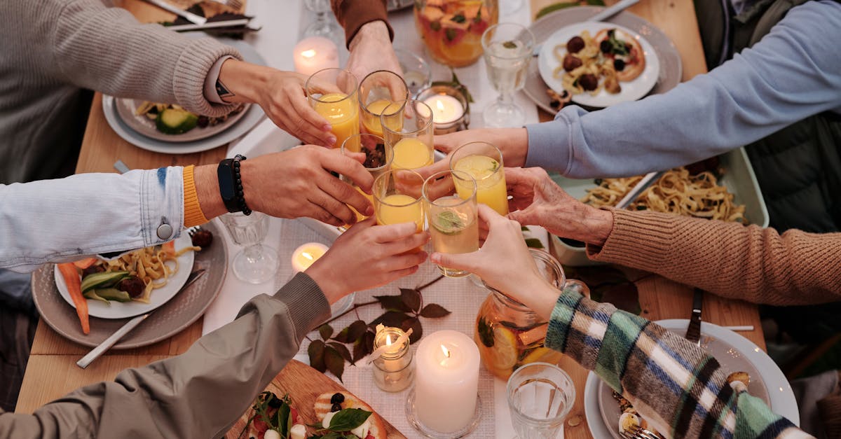 From above of crop friends enjoying dinner with candles while cheering with glasses of drinks